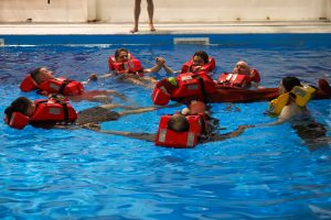 Delegates completing Personal Survival Techniques Marine Course. In swimming pool, forming a ring by holding hands